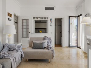 Ein modernes Wohnzimmer mit einer Couch, einem Bett und einem Essbereich, der durch eine offene Tür sichtbar ist.