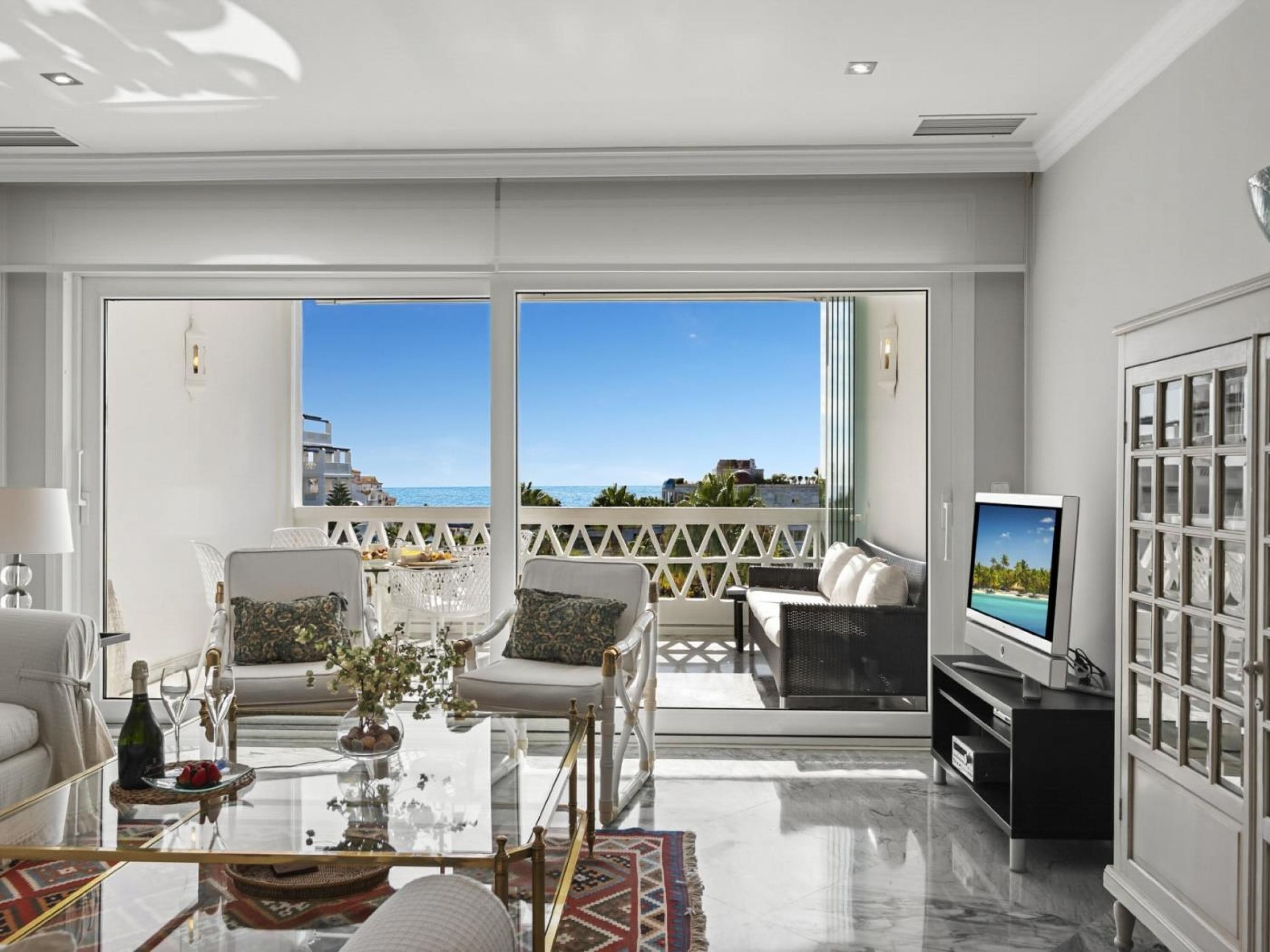 A spacious living room with a balcony, a television, and a glass coffee table.