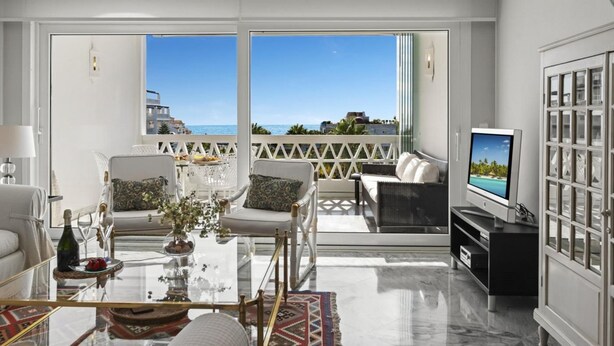 A spacious living room with a balcony, a television, and a glass coffee table. - Vista mar y Piscina en Puerto Ban s (Marbella)