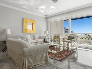 Ein modernes Wohnzimmer mit Sofa, Sesseln, einem Glastisch und Blick auf das Meer.
