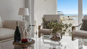 A room with a glass table, a bottle of champagne, glasses, a bowl of fruit, and a vase with flowers. - Vista mar y Piscina en Puerto Ban s (Marbella)