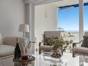 Ein Zimmer mit Glastisch, einer Champagnerflasche, Gläsern, einer Obstschale und einer Blumenvase.