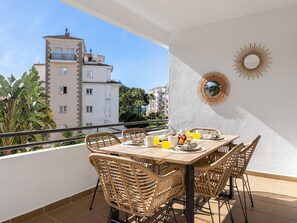 A balcony with a table set for breakfast, wicker chairs, and a view of a building and palm trees. - Apartamento de 2 Dormitorios con Terraza ref 211 (Marbella)