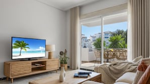 A modern living room with a television displaying a beach scene, a wooden coffee table, a sofa, and a balcony with outdoor furniture. - Apartamento de 2 Dormitorios con Terraza ref 211 (Marbella)