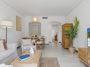 A modern living room with a sofa, coffee table, and a dining area with a table set for two. - Apartamento de 2 Dormitorios con Terraza ref 211 (Marbella)