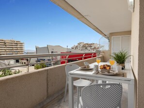 Ein Balkon mit einem Tisch für zwei Personen, einem Blumentopf und Blick auf Gebäude im Hintergrund.