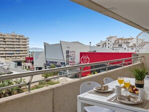 Ein Balkon mit Frühstückstisch, Blick auf eine Stadtlandschaft mit Gebäuden und blauem Himmel.