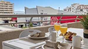 Ein Balkon mit einem Tisch, gedeckt für ein Frühstück, darunter Gebäck, ein Glas Orangensaft und eine Tasse.