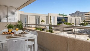 Ein Balkon mit Frühstückstisch, mit Blick auf ein modernes Gebäude mit Solaranlage und einem Berg im Hintergrund.