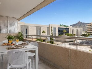 Ein Balkon mit Frühstückstisch, mit Blick auf ein modernes Gebäude mit Solaranlage und einem Berg im Hintergrund.
