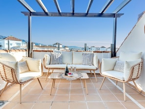 A terrace with wicker furniture, a table with a bottle and glasses, and a view of buildings in the background. - Precioso Tico con Vistas al mar ref 771 (Marbella)