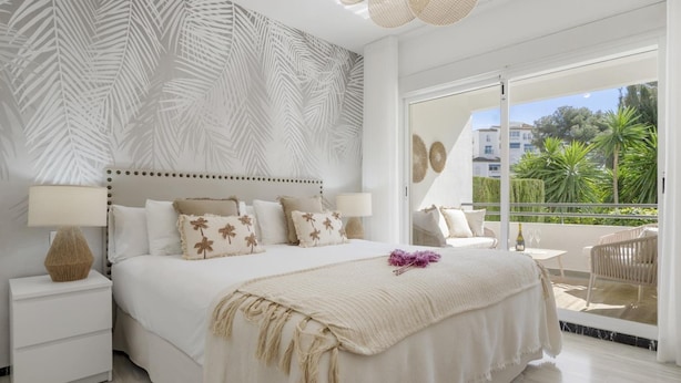 A bedroom with a bed, nightstands, a balcony with outdoor furniture, and a view of greenery. - Medina Garden 201 in Puerto Ban s - Marbella (Marbella)