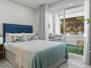 Ein Schlafzimmer mit einem großen Bett, einem Schreibtisch und Blick auf einen Balkon mit Grünpflanzen.
