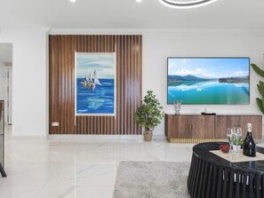 Ein modernes Wohnzimmer mit einem großen Flachbildfernseher, einem gerahmten Gemälde, einer Topfpflanze und einem Marmorboden.