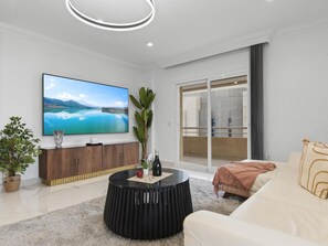 Ein modernes Wohnzimmer mit Flachbildfernseher, rundem Couchtisch, Sofa und großem Fenster.