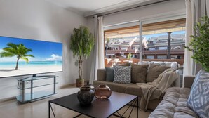 Ein modernes Wohnzimmer mit einem großen Flachbildfernseher, einem Glastisch und einer gemütlichen Couch.