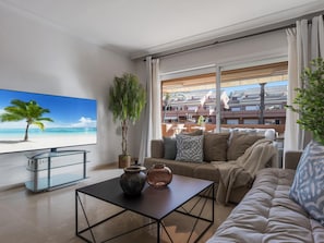 Ein modernes Wohnzimmer mit einem großen Flachbildfernseher, einem Glastisch und einer gemütlichen Couch.