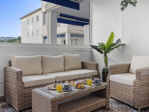 A balcony with a wicker sofa, a coffee table with breakfast items, and a potted plant.