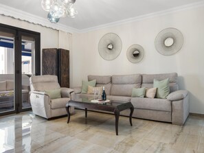 Ein Wohnzimmer mit einer Couch, Sesseln, einem Glastisch und dekorativen Wandspiegeln.