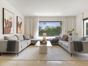 A modern living room with a sectional sofa, a glass coffee table, and a view of greenery outside. - Villa Byrons in Marbella (Marbella)