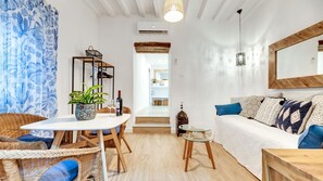A modern living room with a white sofa, wicker chairs, a glass coffee table, and a dining table with a plant and wine glasses. - Heritage Hideaway A Step Back In Time (Marbella)