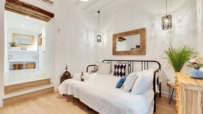 A bedroom with a bed, bedside table, lamp, mirror, and a view of the bathroom. - Heritage Hideaway A Step Back In Time (Marbella)