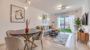 A modern living room with a sofa, coffee table, and dining table. There are two chairs, a vase with dried plants, and artwork on the walls. - Puerto Banus Serenity Retreat (Marbella)
