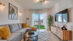 A modern living room with a grey sofa, a coffee table, a TV, and a balcony with a view of buildings. - Puerto Banus Serenity Retreat (Marbella)