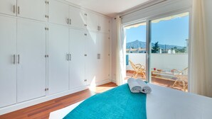A bedroom with a large wardrobe, a bed with a blue blanket, and a balcony with wicker furniture. - Los Angeles Beach Front Villa (Marbella)