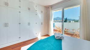 Ein Schlafzimmer mit großem Kleiderschrank, einem Bett mit blauer Decke und einem Balkon mit Korbmöbeln.