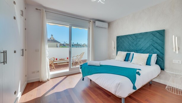 A bedroom with a large bed, a view of the outside, and a balcony with chairs. - Los Angeles Beach Front Villa (Marbella)