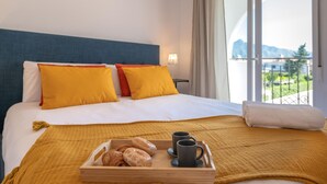 A hotel room with a bed, pillows, a tray with pastries and coffee cups, and a view of mountains through the window. - Los Angeles Beach Front Villa (Marbella)