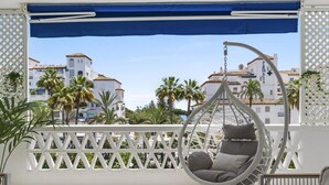 A balcony with a hanging chair, a bottle of champagne, and a view of buildings and palm trees. - Beach Puerto Ban s 3 Br Apartment (Marbella)