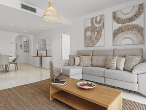 A modern living room with a sectional sofa, a coffee table, and decorative wall art. - Beach Puerto Ban s 3 Br Apartment (Marbella)