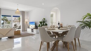 A modern dining area with a white table set for four, surrounded by grey upholstered chairs with wooden legs. - Beach Puerto Ban s 3 Br Apartment (Marbella)