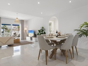 A modern dining area with a white table set for four, surrounded by grey upholstered chairs with wooden legs. - Beach Puerto Ban s 3 Br Apartment (Marbella)