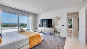 A modern bedroom with a large bed, a TV, and a view of the sea. - Villapadierna Solstice Sanctuary Villa (Estepona)