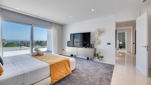 Ein modernes Schlafzimmer mit einem großen Bett, einem Fernseher und Blick aufs Meer.