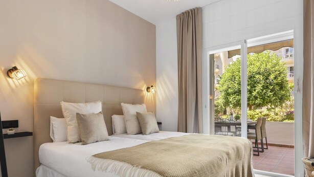 A bedroom with a large bed, two wall-mounted lights, a view of the outdoors through a sliding door, and a balcony with a table and chairs. - Fabuloso Apartamento Junto a la Playa (Marbella)