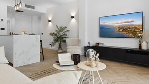 A modern living room with a large flat-screen TV, a marble kitchen island, a comfortable sofa, and a potted plant. - Fabuloso Apartamento Junto a la Playa (Marbella)
