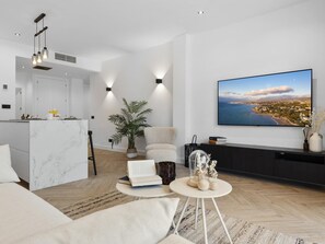 Ein modernes Wohnzimmer mit großem Flachbildfernseher, einer Marmorkücheninsel, einer bequemen Couch und einem Topfpflanzen.