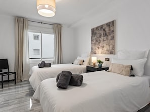 Ein Hotelzimmer mit zwei Betten, einem Schreibtisch, einem Stuhl, einem fenster mit Vorhängen und einem Bild an der Wand.
