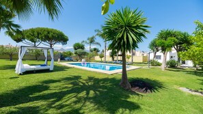 A pool area with a bed and a canopy, surrounded by grass and palm trees. - Guadalmina Cozy Sea Front Villa (Estepona)