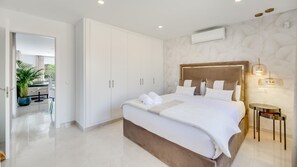 A modern bedroom with a large bed, white wardrobe, and a potted plant. - Guadalmina Cozy Sea Front Villa (Estepona)