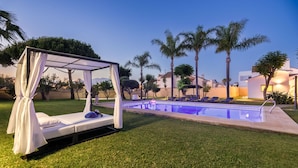 Ein Poolbereich mit Liegebett, Palmen und einem gut beleuchteten Pool.