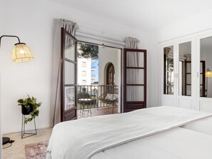 Ein Schlafzimmer mit einem Bett, einer Topfpflanze, einer Lampe und Blick auf den Balkon.