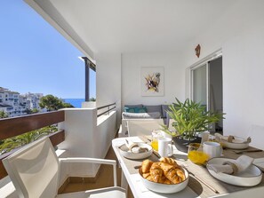 A balcony with a table set for breakfast, a sofa, and a view of the sea. - 1 Dormitorio en Medina Garden (Marbella)