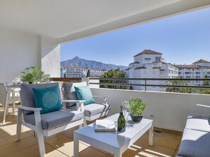 A balcony with white furniture, a small table, and a potted plant. - 1 Dormitorio en Medina Garden (Marbella)