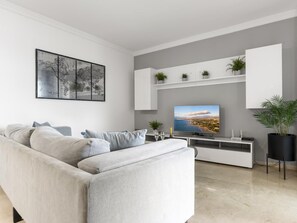 Ein modernes Wohnzimmer mit einem grauen Sofa, einem Flachbildfernseher und einer Weltkarte als Wandbild.