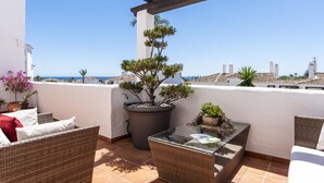 Un balcon agrémenté de meubles en osier, d’un arbre en pot et offrant une vue sur la mer.